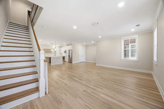A spacious room with wooden flooring and a staircase on the left side.