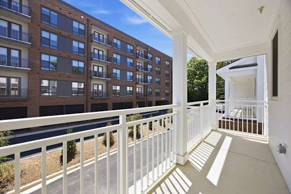 A balcony with white railings overlooks a parking lot and a building.