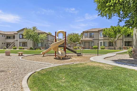 A playground with a yellow slide in the middle of a grassy area at Adiamo Palm Valley, Goodyear, 85395