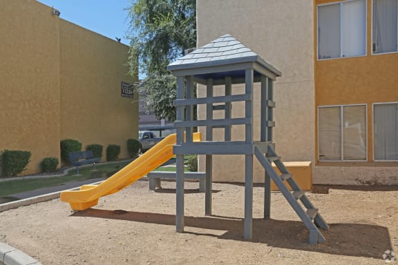 a playground with a yellow slide in front of a building