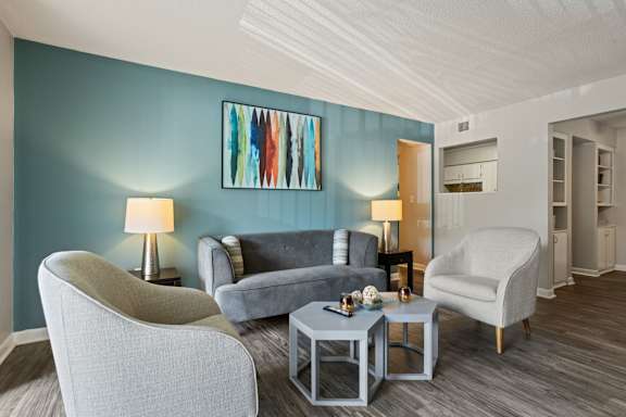 A living room with a grey sofa, a grey armchair, a grey coffee table, and a painting on the wall.