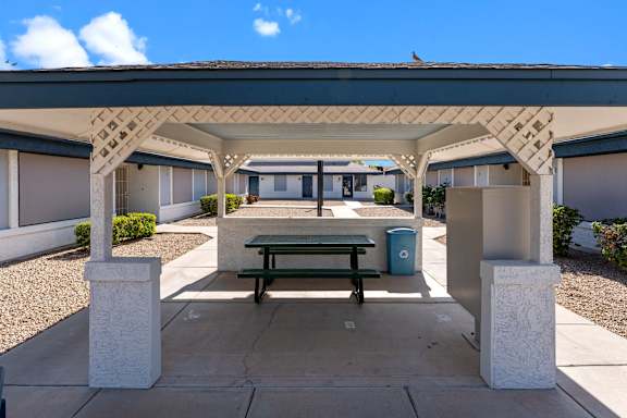 A covered patio area with a bench and a trash can.
