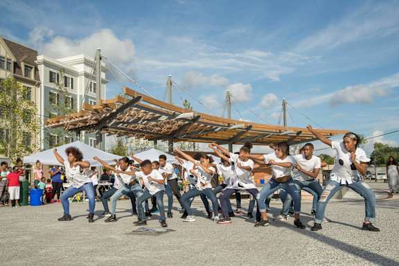 A group of people are dancing in front of a wooden structure.