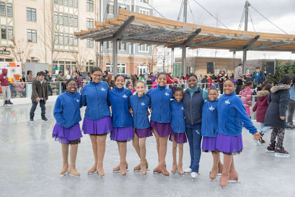 A group of people in blue and purple uniforms are ice skating.