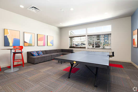 A room with a grey sofa, a red chair, a table and a ping pong table.