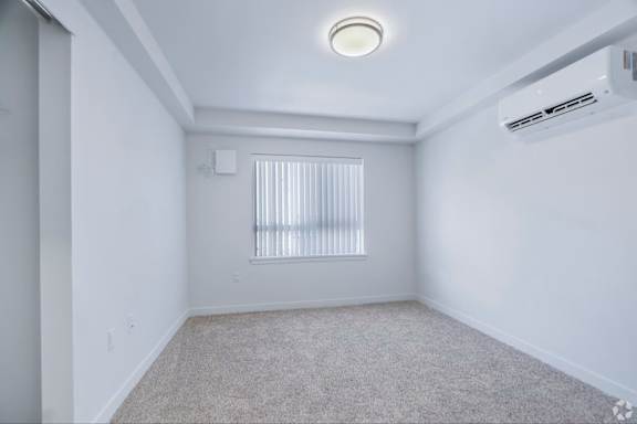 A white room with a window covered by white blinds and a carpet on the floor.