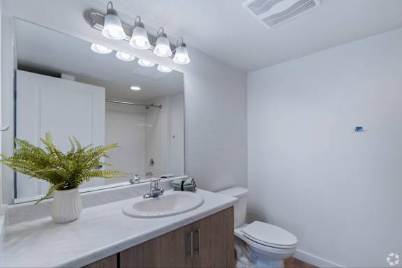 A white bathroom with a toilet, sink, mirror, and lights.