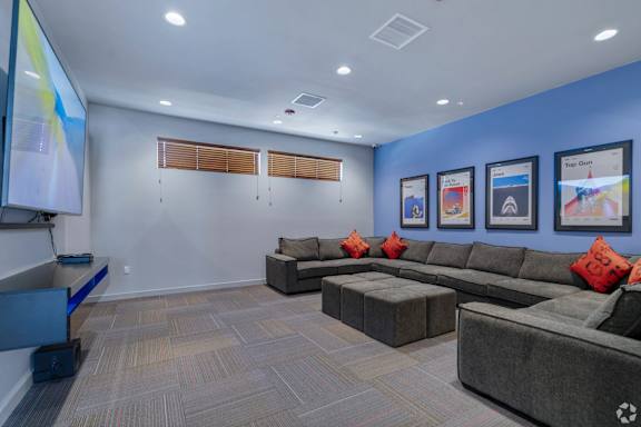 A room with a grey carpet and a grey couch with red pillows.