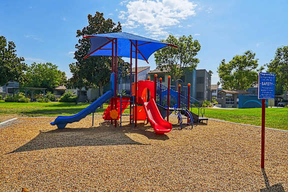 A playground with a blue umbrella and a red slide.