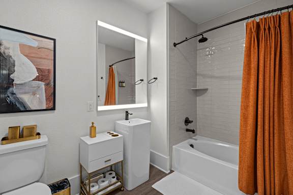 a bathroom with a white tub and sink and a orange shower curtain