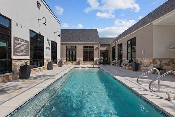 a swimming pool with chairs around it in front of a house