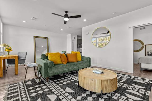 A living room with a green couch and a round mirror on the wall.