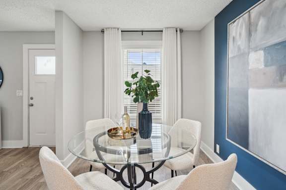A dining room with a glass table and white chairs.