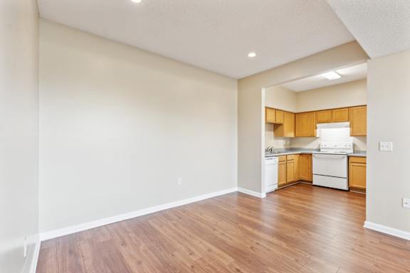 A kitchen with wooden cabinets and white appliances is visible through a doorway.