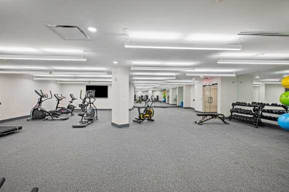 A gym with exercise equipment and a grey carpet.