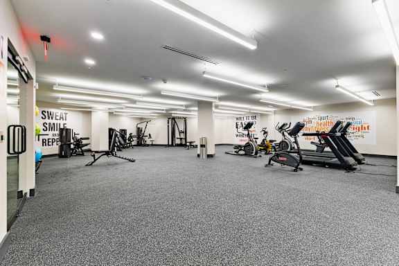 A gym with a variety of equipment including treadmills, stationary bikes, and weights.