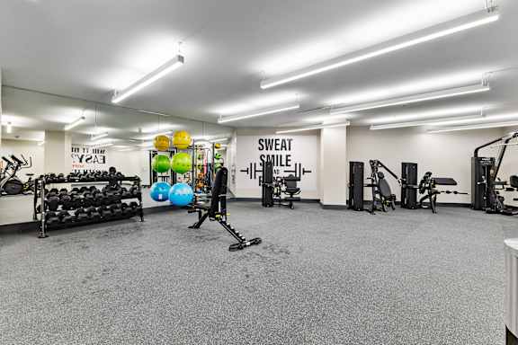 A gym with a variety of equipment including a bench press, a squat rack, and a rowing machine.