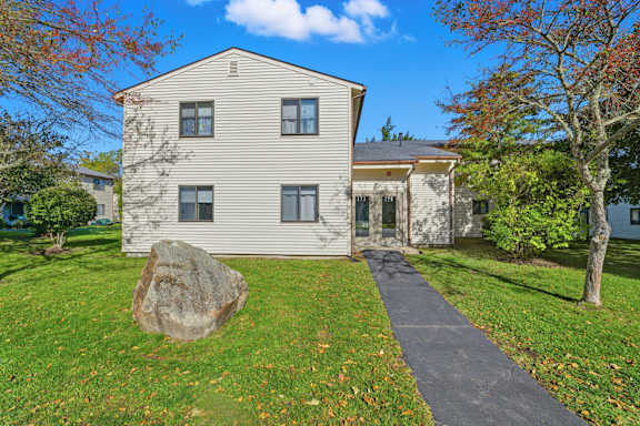A two story house with a blue door and a tree in front at Hidden Brook Apartment Homes Apartments, New Bedford, MA, 02740