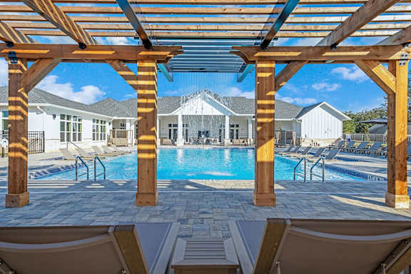 A wooden pergola over a swimming pool with lounge chairs underneath.