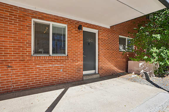 A red brick house with a grey door and a window with blinds.