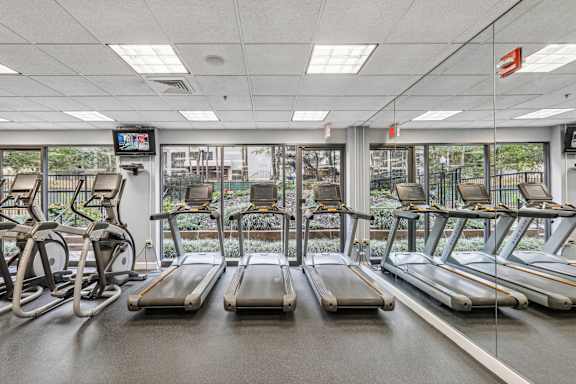 a gym with cardio machines and a window view of a city