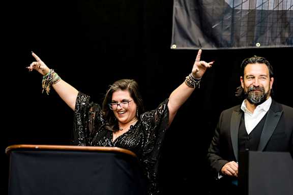 A woman with her right hand raised is standing behind a podium.