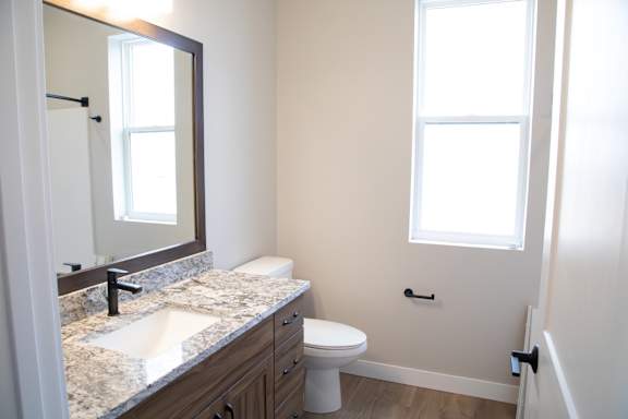 A bathroom with a sink, mirror, toilet and a window.