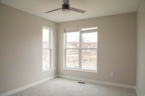 A room with a ceiling fan and two windows.