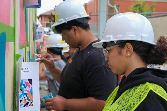 A group of people wearing hard hats are looking at a poster with the number 3 on it.