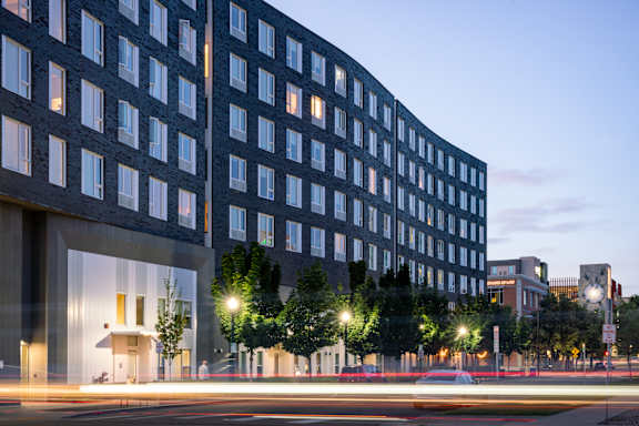 A modern building with a lot of windows is shown with a blurred street in the foreground.