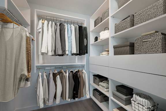 A white closet with clothes hanging and baskets on shelves.