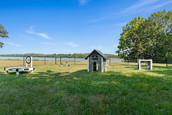A small building sits in a field with a picnic table and a fence in the background.