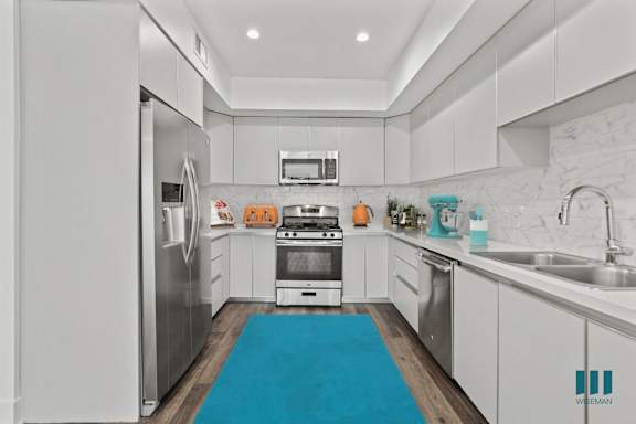 a white kitchen with stainless steel appliances and a blue rug