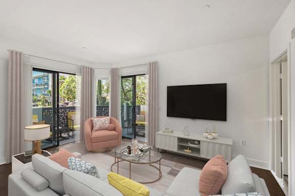A living room with a grey couch, a yellow pillow, a television and a glass table.