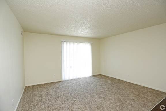 Large carpeted living room with sliding patio door and blinds