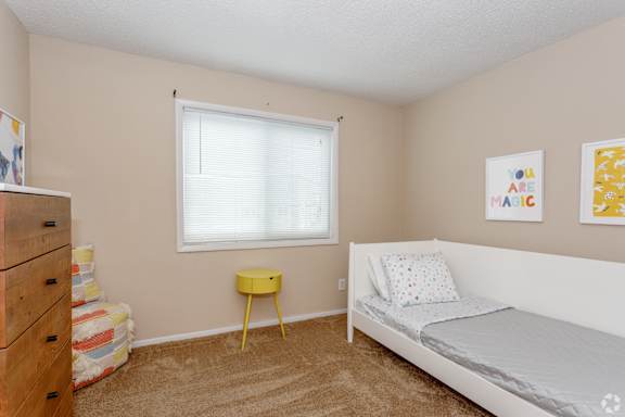 Large carpeted bedroom with white daybed with pastel sheets covering it and paintings on the grey wall