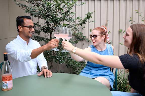 A man in a white shirt is toasting with two women at a table.