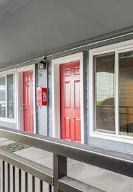 A white window with a red door to the left and a black railing below.