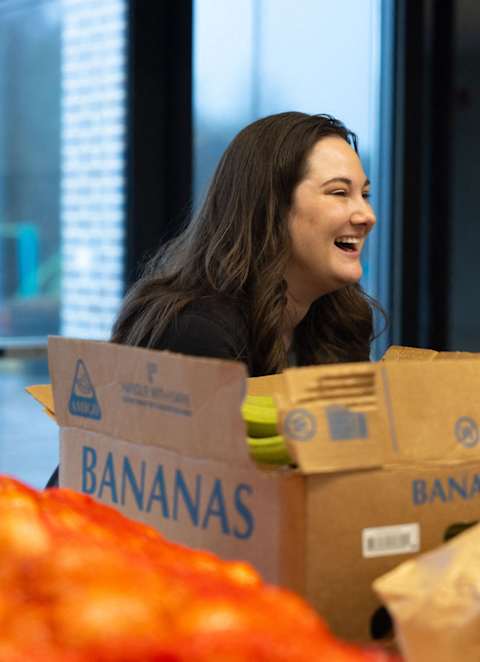 a woman smiles as she sits next to a box of bananas