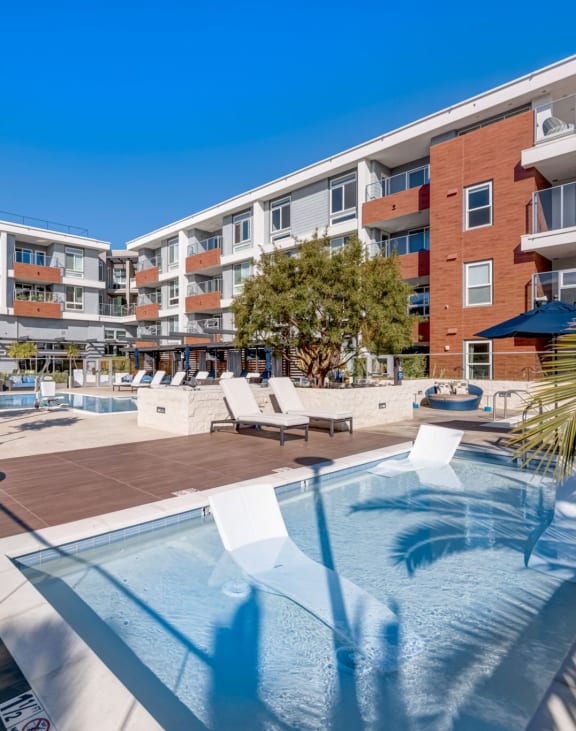 Large pool with lounge chairs and umbrellas in front of an apartment building at One Uptown Newport.
