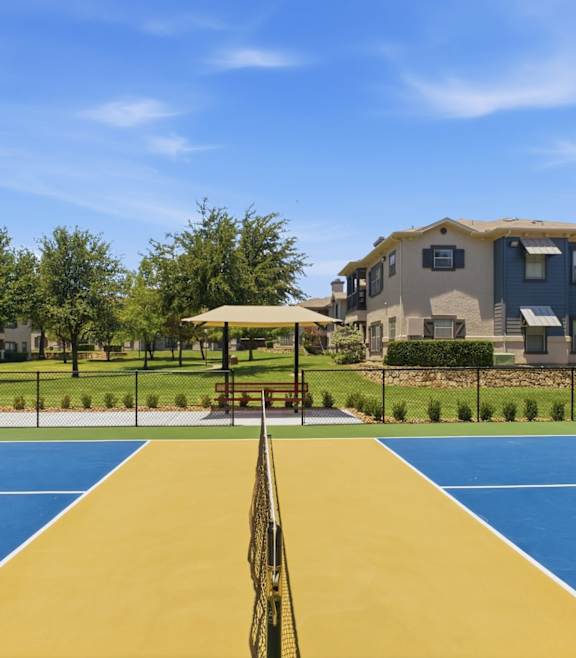 A playground with a blue and yellow surface and a black fence.