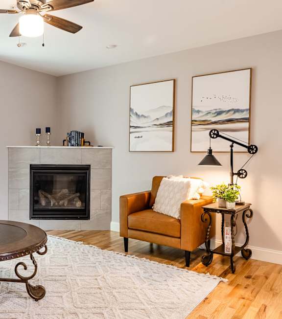 A living room with a fireplace, a chair, a table, and a plant.