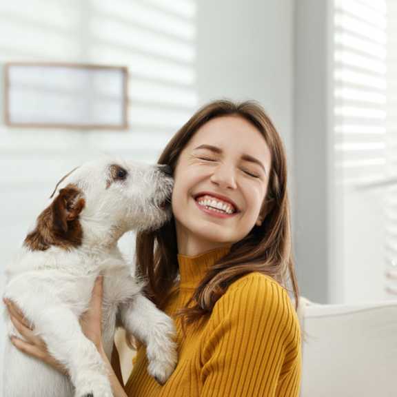 A woman in a yellow sweater is holding a white dog with brown spots.