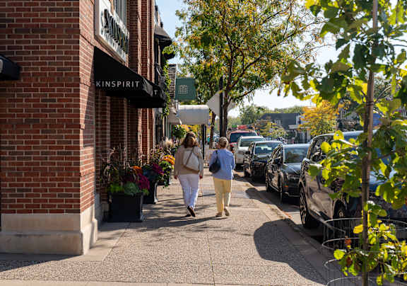 A woman walking down a sidewalk past a store with a sign that says "KINSPIRIT".