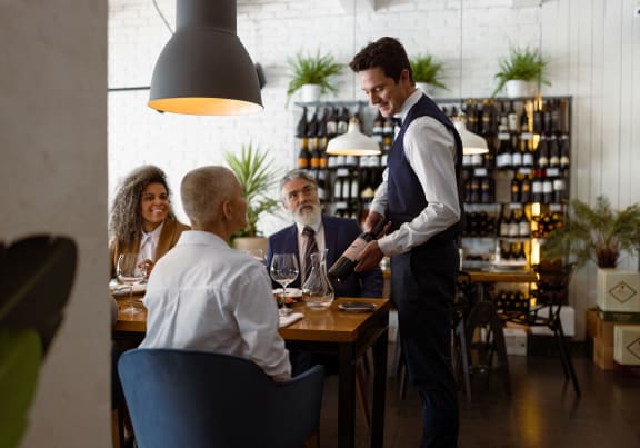 a waiter pouring a glass of wine for a group of people sitting at a table in a