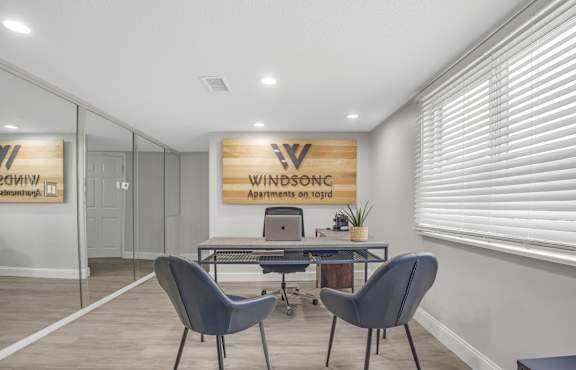 A room with a desk and chairs with a sign that says Windsonic Apartments on the wall.