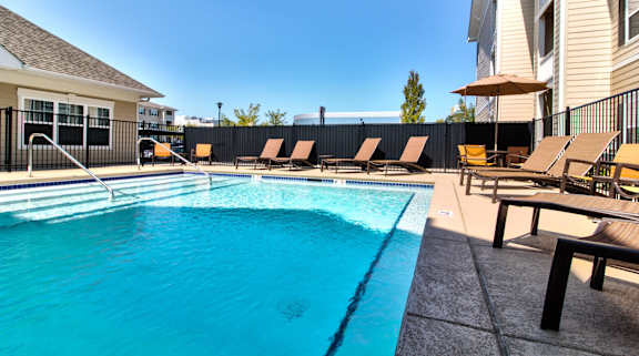 A swimming pool with sun loungers and a building in the background.