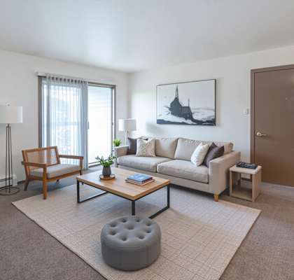A living room with a couch, chair, ottoman, and a painting on the wall.
