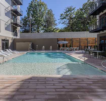 A large outdoor swimming pool surrounded by a stone patio and lounge chairs.