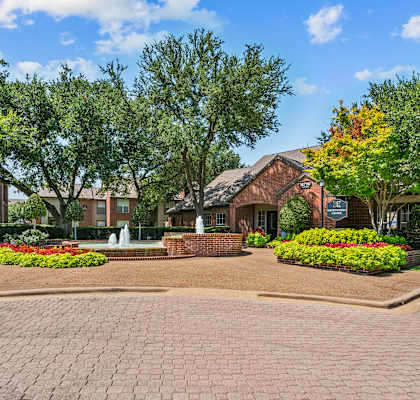 a fountain sits in front of a brick building with trees in the background